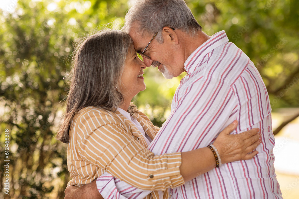 Fototapeta premium Cheerful european mature couple hugging, want to kiss, enjoy spare time together in park at summer weekend