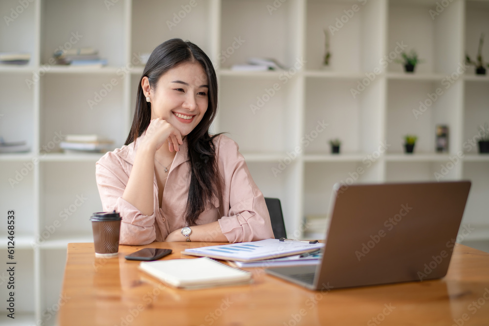 Happy smiling business woman working with laptop computer with paperwork at desk in a modern office, business finance technology concept.