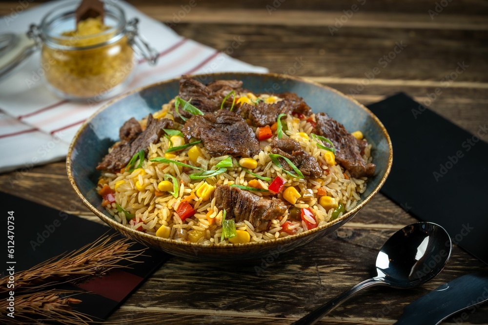 Fried rice dish with beef pieces and cutlery on a wooden table