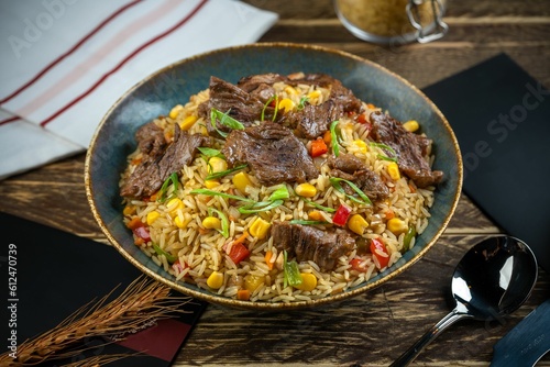 Fried rice dish with beef pieces and cutlery on a wooden table with blur gray cloth