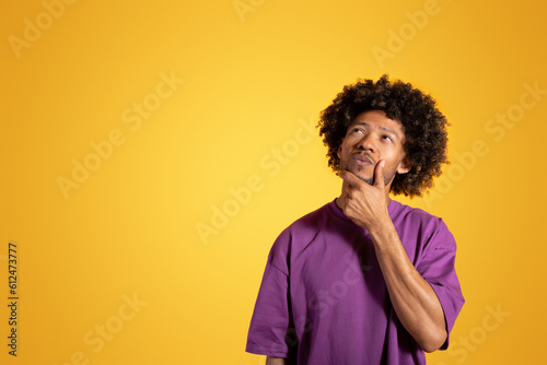 Serious pensive black adult curly man in purple t-shirt, thinks, look at copy space © Prostock-studio
