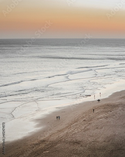 Aerial view of people walking on sandy beach during sunset on a cold windy day