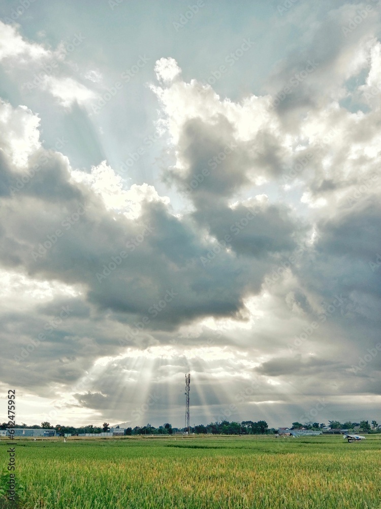 Vertical shot of the sun shining through a huge cloudscape over a green field