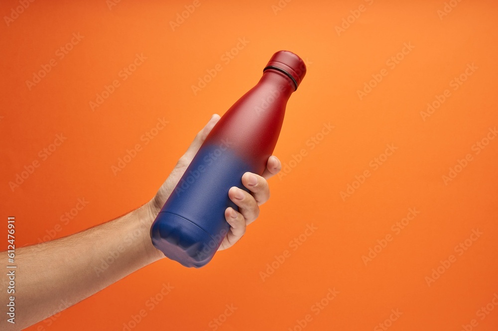 Hand holding a colorful thermal bottle on an orange background Hand holding a colorful thermal bottle on an orange background