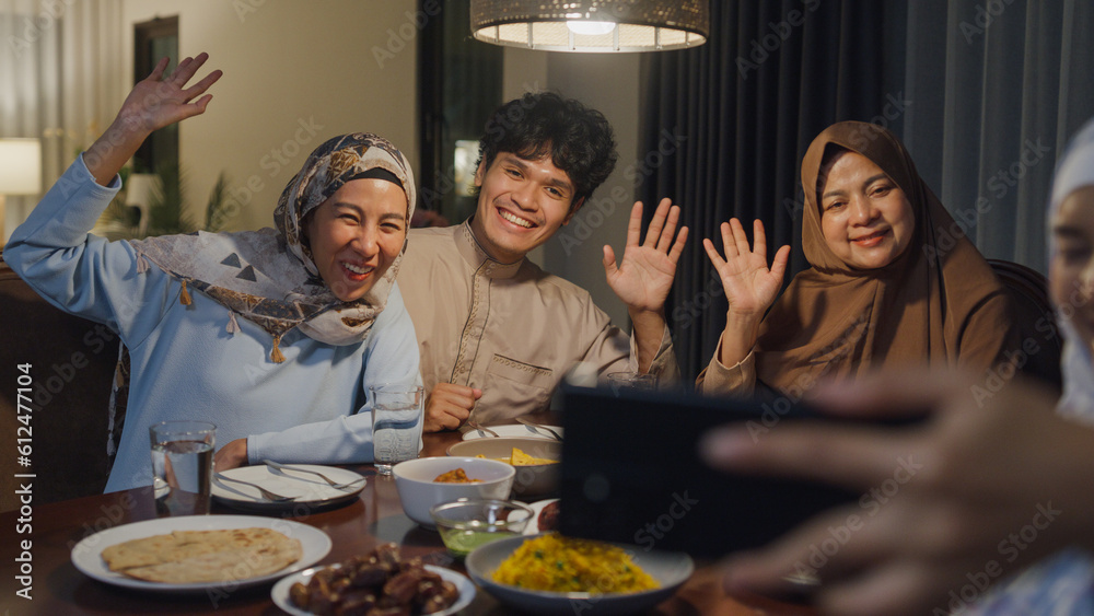 Happy Asian muslim family celebrate long distance with cousin use cell phone video call online Ramadan dinner together at home. Two generation celebration of Eid al-Fitr togetherness at home.