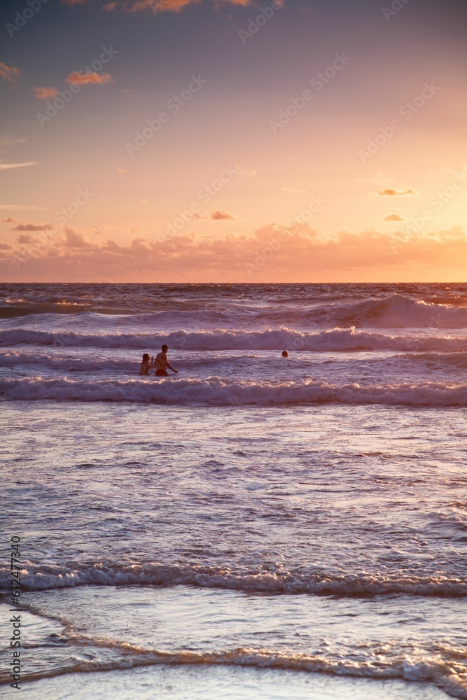 Vertical shot of people having fun in sea at sunset