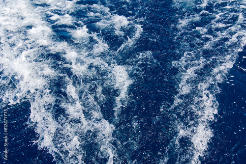 Abstract blue sea water with white waves. Blue sea texture with waves and foam. Rough deep turquoise and blue Mediterranean sea. Sea water top view.