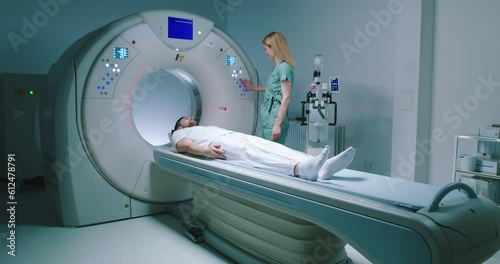 Male patient lies at TC scanner bed. Man goes out of MRI capsule. Female doctor dressed up in uniform have talk with patient. Medical worker smiling and pushes buttons of MRI capsule. photo