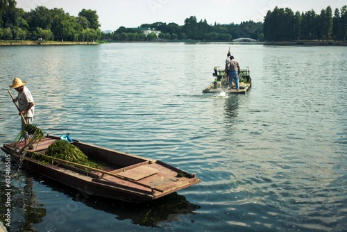 Chinese boaters clean the lake from algae in the park © Zhou Chenxiao/Wirestock Creators