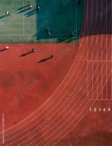 Quadro su tela Aerial top view of a brown running track and a green court with people on a sunn