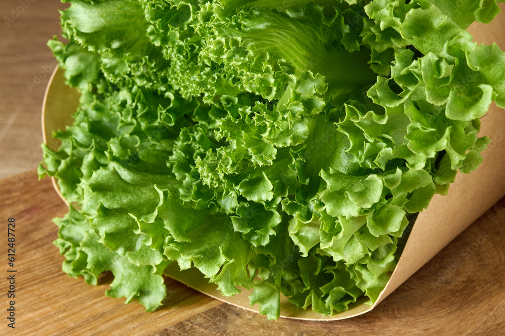 Fresh green lettuce in cartoon box laying on wooden cutting board Fresh green lettuce in cartoon box laying on wooden cutting board