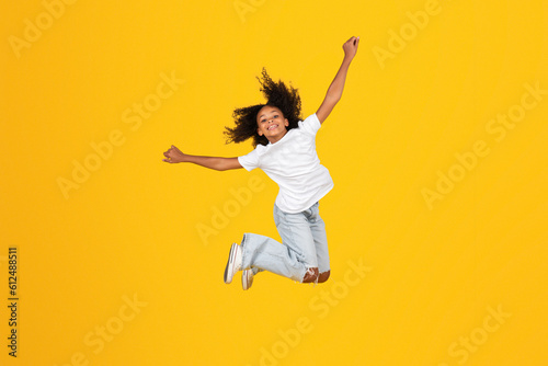 Cheerful curly teen black schoolgirl in white t-shirt has fun, jumping, freezes in air, enjoy freedom