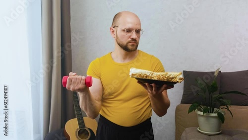 The man lifts a dumbbell in his right hand and a plate with a calorie left in his other hand, looks at them and shakes his shoulders questionably. Concept of choice and willpower in weight loss photo