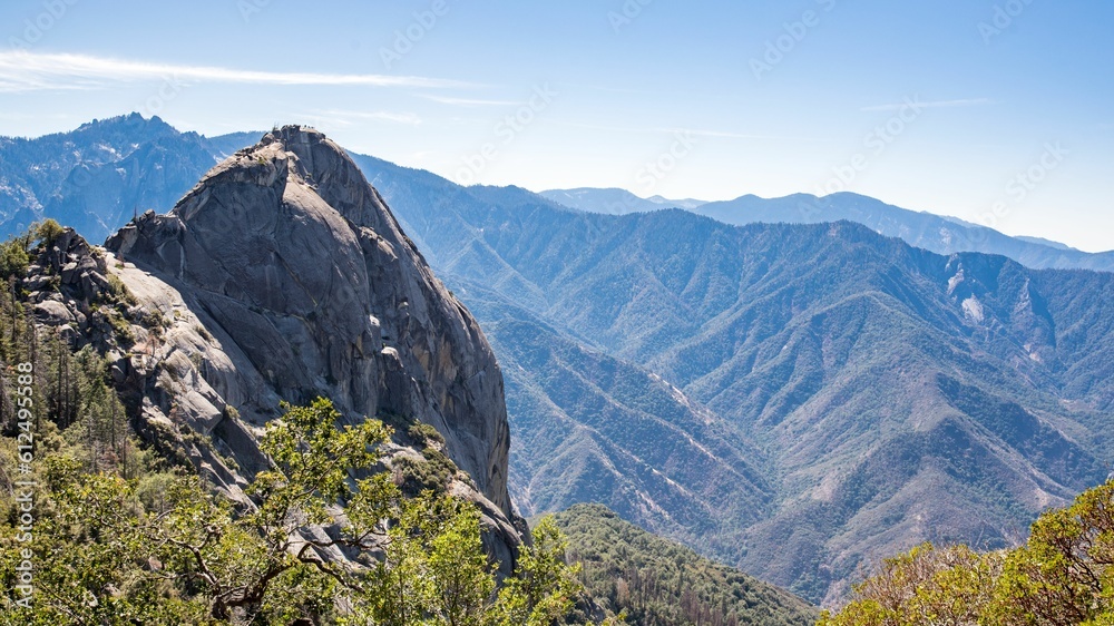 Scene of the rocky mountain range with some plants illuminated by sun ray rays under a blue sky