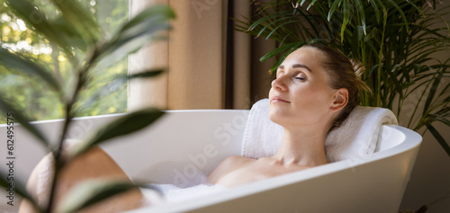 Obraz na płótnie woman relaxing in bathtub with eyes closed in bathroom with green tropical plants
