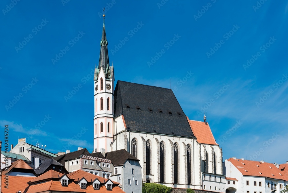 Fototapeta premium Church of St. Vitus surrounded by red roof buildings under a blue sky in Cesky Krumlov, Czechia