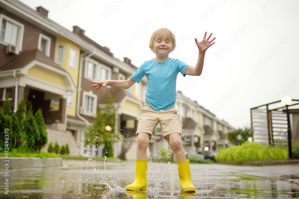 Little boy wearing yellow rubber boots jumping in puddle of water on ...