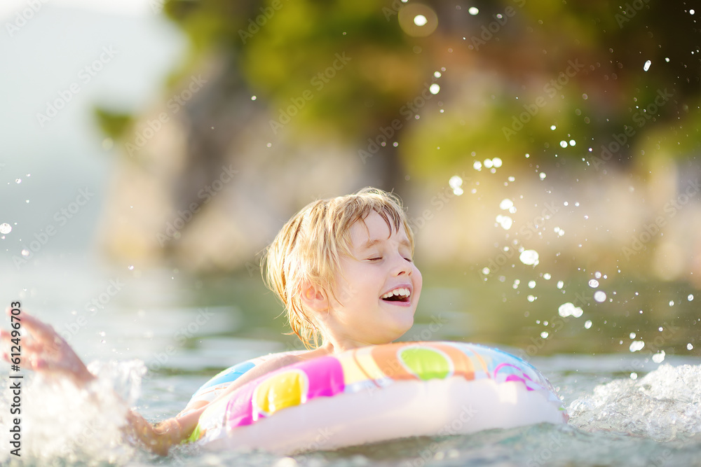 Little boy swimming with colorful floating ring in sea on sunny summer day. Cute child playing in clean water. Family and kids resort holiday during summer vacations.