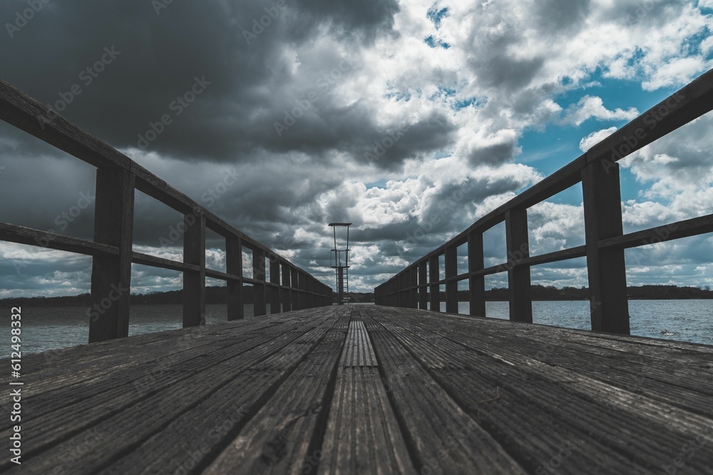 Landscape scene of a long wooden pier under dramatic cloudy sky