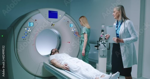Man is lying down at TC scanner capsule. Medical pushes buttons and prerares for tomography examination. Female doctor checked process and goes out of room. Preparing for magnetic resonance imaging. photo