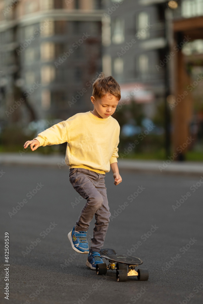 Fototapeta premium Little boy learning to skateboard at sunset