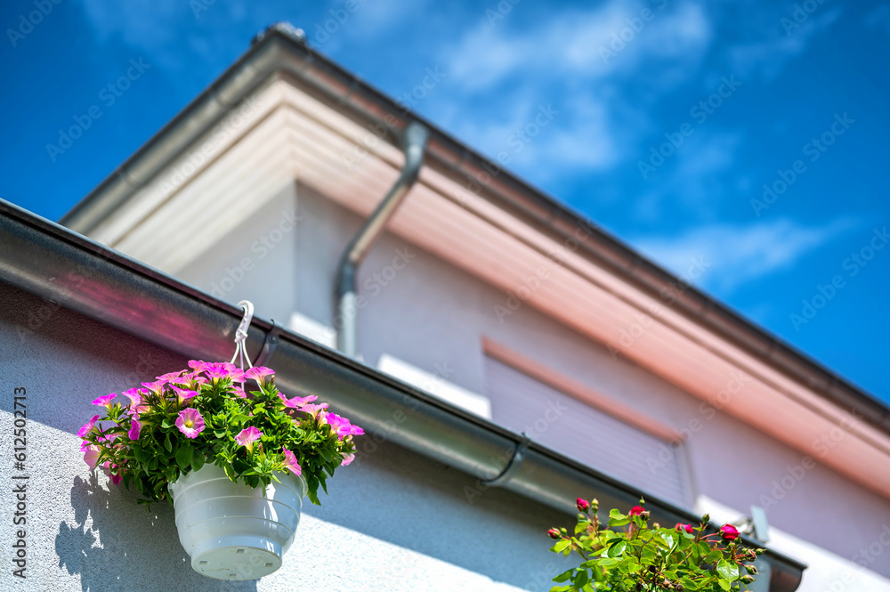 Fototapeta premium Dachentwässerung an einem Wohnhaus mit dekorativen Blumenampeln