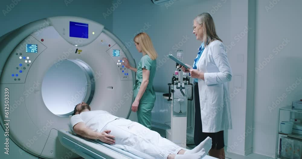 Man is preparing for undergoes magnetic resonance tomography. Medical worker in blue uniform adjusts capsule of MRI examination. Female doctor manages the process of patient's scanning. Man is preparing for undergoes magnetic resonance tomography. Medical worker in blue uniform adjusts capsule of MRI examination. Female doctor manages the process of patient's scanning.