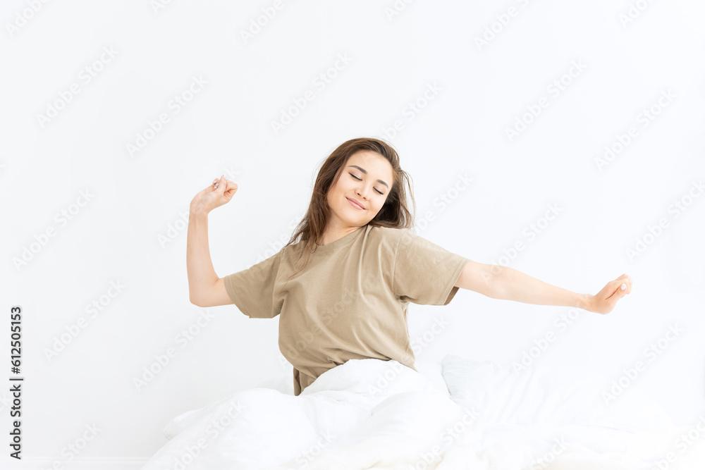 Beautiful girl waking up and stretching in white linens in bright bedroom flooded with sunlight. Happy morning awakening and feeling good. Beautiful girl waking up and stretching in white linens in bright bedroom flooded with sunlight. Happy morning awakening and feeling good.