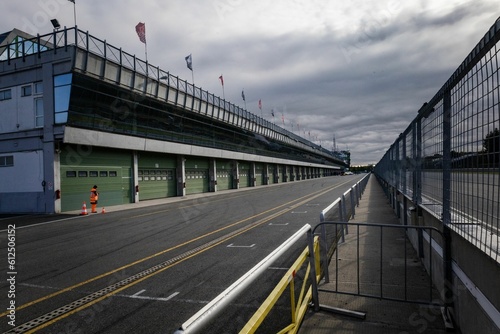 Принти на полотні Motor racing of asphalt road by a building with flags and metal fence under clou