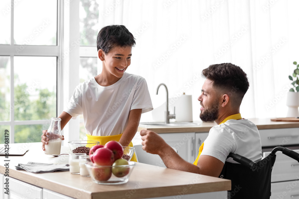 Little boy and his father in wheelchair having breakfast at home
