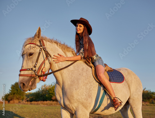 Beautiful young woman with long hair in cowboy hat with the brown horse outdoors
