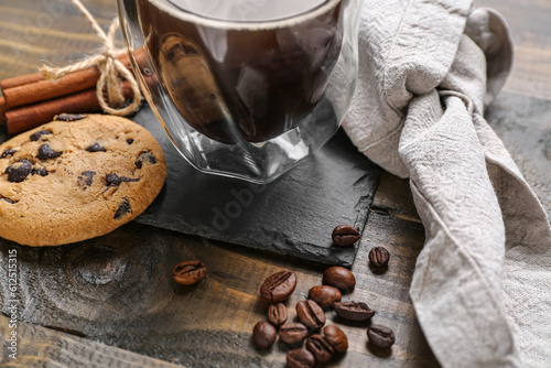 Drink coaster with cup of coffee, cookie and beans on wooden table