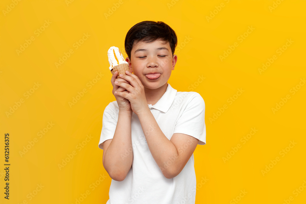 asian little boy of ten years old licks ice cream cone on yellow isolated background asian little boy of ten years old licks ice cream cone on yellow isolated background