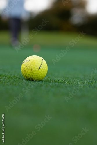 Vertical closeup shot of a yellow golf ball on the green golf course on an isolated background