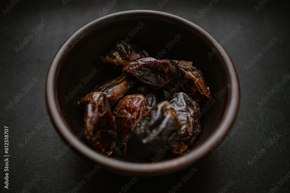Dried dates in a clay bowl on a black table. Still life with dried fruits. Date palm fruits. A healthy snack. Low-calorie dessert. Sweet diet food. Rural scene. Vegetarian food. Dried dates in a clay bowl on a black table. Still life with dried fruits. Date palm fruits. A healthy snack. Low-calorie dessert. Sweet diet food. Rural scene. Vegetarian food.