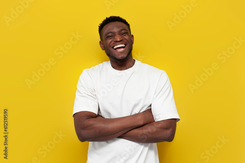 happy african american man in white t-shirt stands with his arms crossed on yellow isolated background