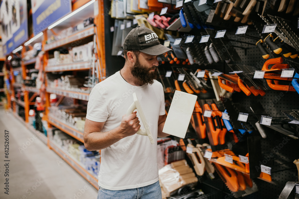 Young handsome man with a beard in casual clothes in a construction hypermarket chooses tools Young handsome man with a beard in casual clothes in a construction hypermarket chooses tools