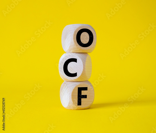 OCF - Operating Cash Flow symbol. Wooden cubes with words OCF. Beautiful yellow background. Business and OCF concept. Copy space.