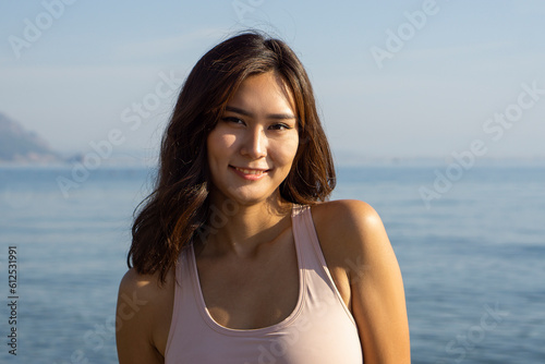 Charming happy Asian woman smiling at camera while standing in front of amazing mountain landscape © Tetiana