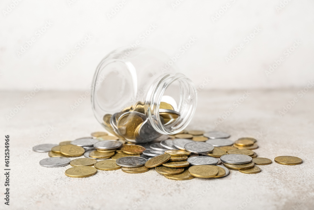 Overturned jar with coins in beige grunge table. Savings concept Overturned jar with coins in beige grunge table. Savings concept
