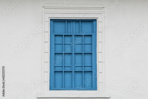 Closeup of the vintage blue window with bars and a white patterned frame on a white concrete wall © Jessica Hu/Wirestock Creators