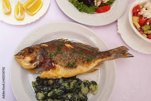 Balkan cuisine. Grilled fish ( sea bream ) with green leafy vegetables on white plate photo