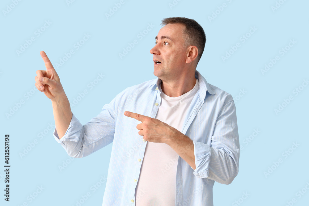 Shocked mature man pointing at something on blue background Shocked mature man pointing at something on blue background