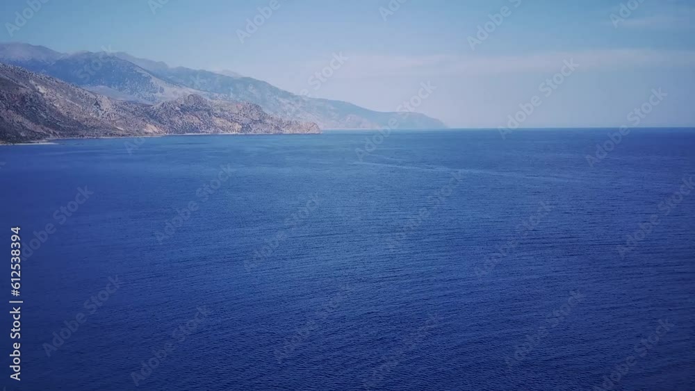 Aerial view of a blue sea surface, with the rocky coast in the background, and a cloudy sky Aerial view of a blue sea surface, with the rocky coast in the background, and a cloudy sky