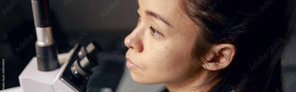 Thoughtful Asian woman in uniform with modern microscope at workplace in hospital laboratory Thoughtful Asian woman in uniform with modern microscope at workplace in hospital laboratory