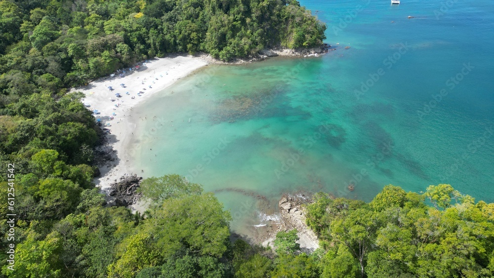 Aerial shot above a beach surrounded by tropical trees in front of an azure sea
