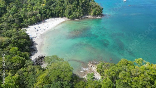 Aerial shot above a beach surrounded by tropical trees in front of an azure sea