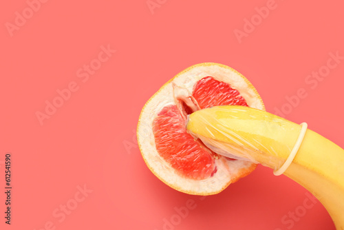 Banana with condom and half of grapefruit on red background. Sex concept
