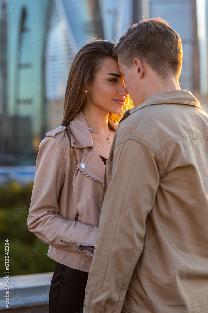 Young happy beautiful loving couple on a surprise romantic date on a rooftop on a Saint Valentine's Day. Attractive man and woman, male and female hugging, kissing. Sunset, skyscrapers urban view