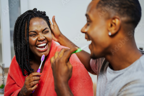 Jovem casal Brasileiro negro sorrindo um para o outro enquanto escovam os dentes juntos no banheiro no dia dos namorados photo